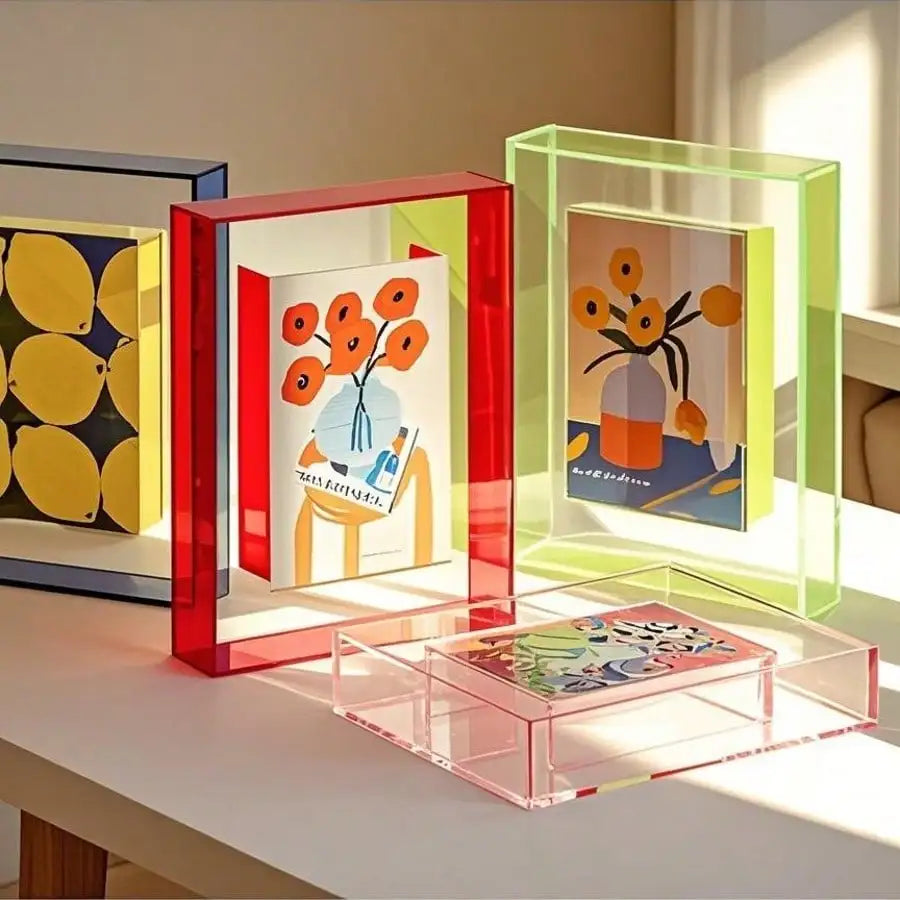 Three vibrant acrylic photo frames in red, green, and yellow display floral and artistic designs on a white table.