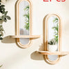 Two wooden geometric wall shelves with oval mirrors and vertical plant accents mounted on a light-colored wall.