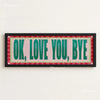 A canvas print featuring the text OK LOVE YOU BYE in green lettering on a pink background with a red plaid border.
