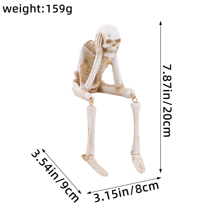 A white resin skeleton skull figurine with elongated limbs and a small decorative element.