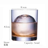 A clear whiskey glass filled with amber liquid and a large ice sphere, shown from the side.