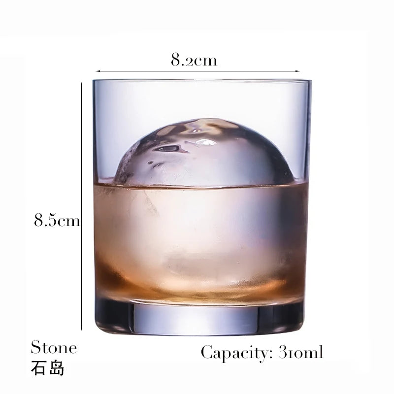 A clear whiskey glass filled with amber liquid and a large ice sphere, shown from the side.
