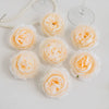 A collection of pale peach and cream silk peony artificial flowers arranged on a white surface.