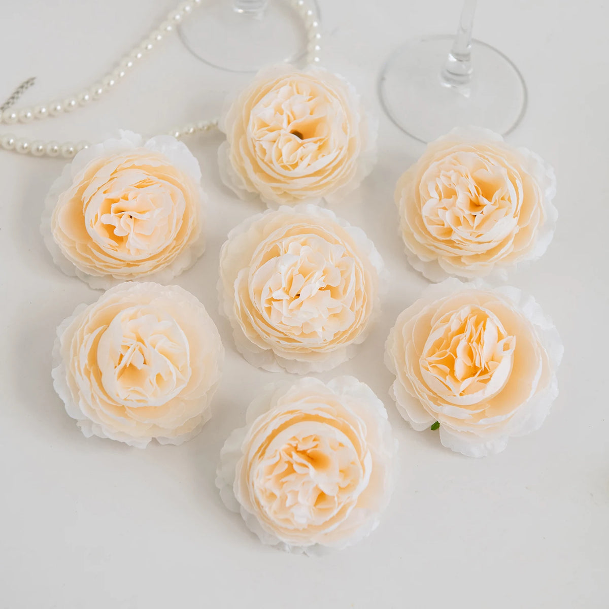 A collection of pale peach and cream silk peony artificial flowers arranged on a white surface.