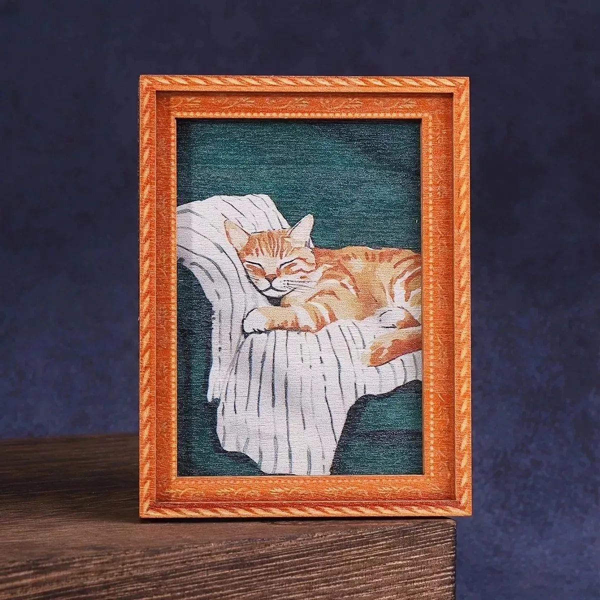 Pintura al óleo de un gato atigrado naranja descansando sobre tela blanca, enmarcado en madera.
