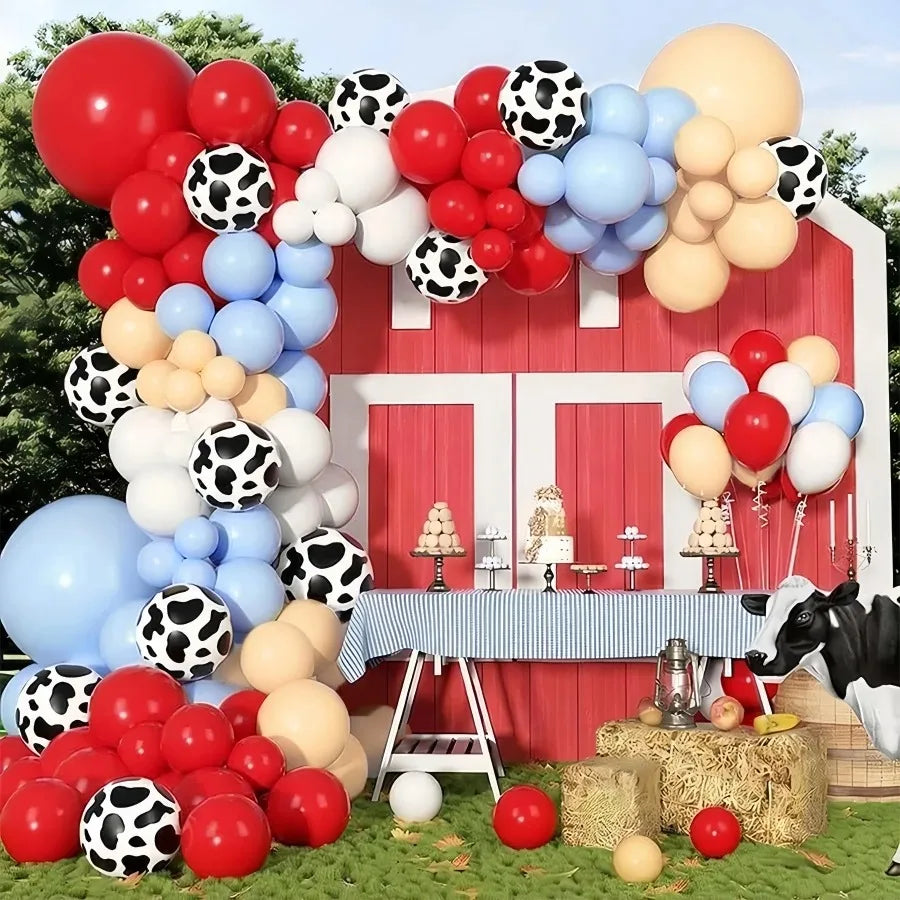 A vibrant balloon garland featuring farm animal shapes and colors like red, white, blue, and orange set up in front of a red 