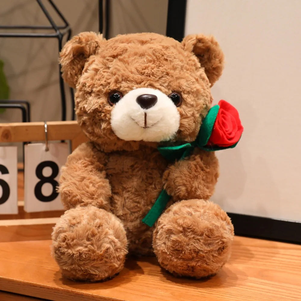 A brown teddy bear plush toy with a red rose ribbon attached, sitting on a wooden surface.