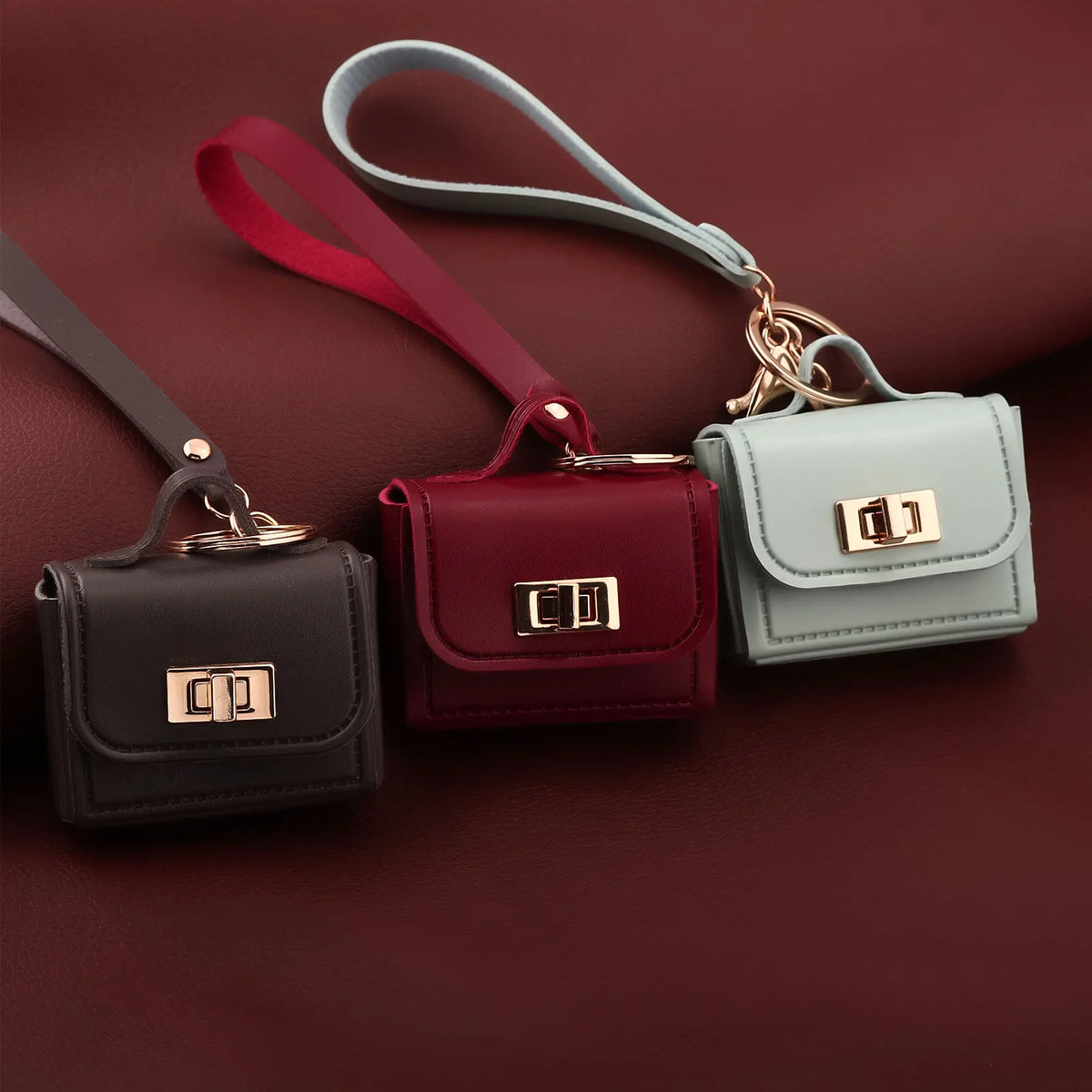A set of mini leather openable bags in maroon, dark green, and light gray with gold hardware.