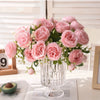 A bouquet of pink silk peony roses displayed in a clear glass vase on a white surface.