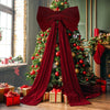 A festive Christmas tree decorated with red ornaments and adorned with a large red velvet bow and long draping streamers.