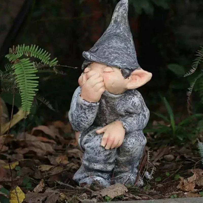 A small statue of a gnome with a pointed hat and gray beard sitting in a garden setting.