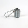 A small, silver pill organizer is attached to a keyring and presented against a white background.