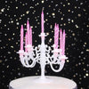 A white cake stand holds nine pink striped birthday candles in elegant holders against a dark background.