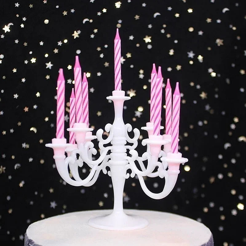 A white cake stand holds nine pink striped birthday candles in elegant holders against a dark background.