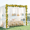 A wedding setup featuring a white draped arch decorated with yellow sunflower garlands and hanging light fixtures.