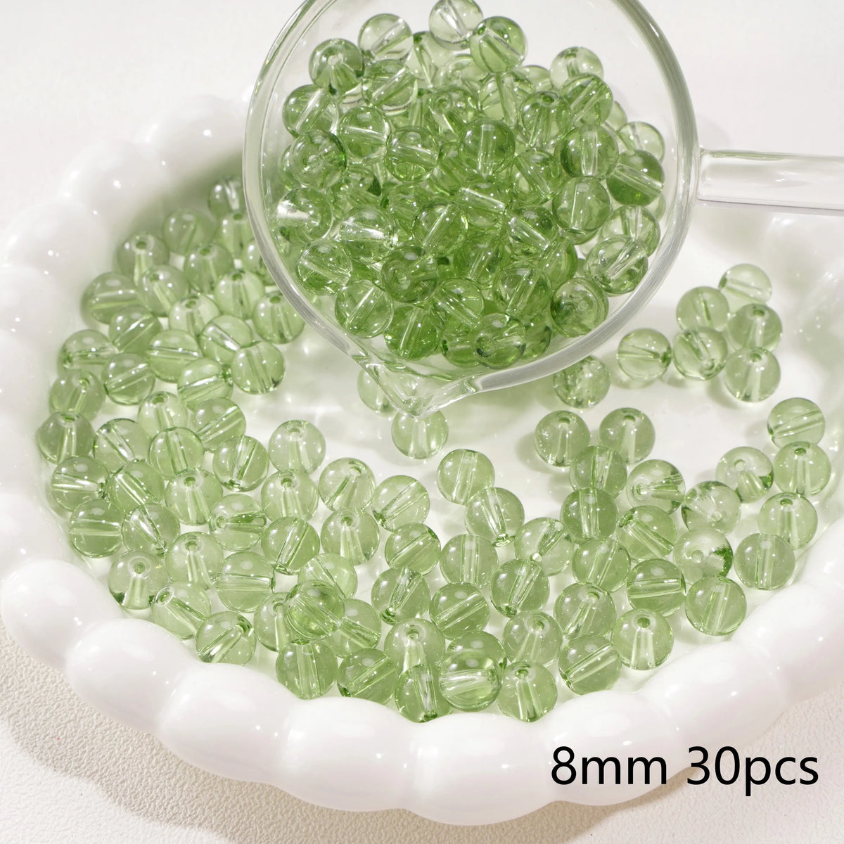 A clear glass dropper shows small green spacer beads scattered on a white dish.