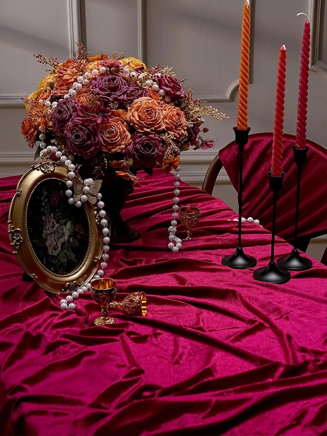A burgundy red velvet rectangular tablecloth set for elegant dining with a floral arrangement and candles.