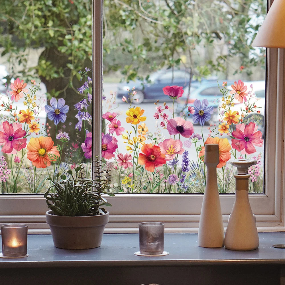 Eine Sammlung farbenfroher Blumen und Schmetterlinge in einem Fenster, mit dekorativen Glasobjekten auf der Fensterbank.