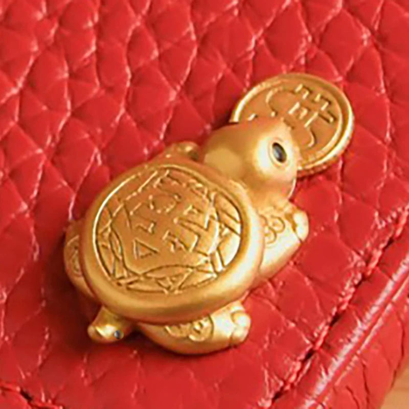 A golden tortoise figurine with a textured shell resting on a red quilted surface.