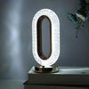 An oval crystal LED table lamp with a gold frame and white diffused light is displayed on a modern surface.
