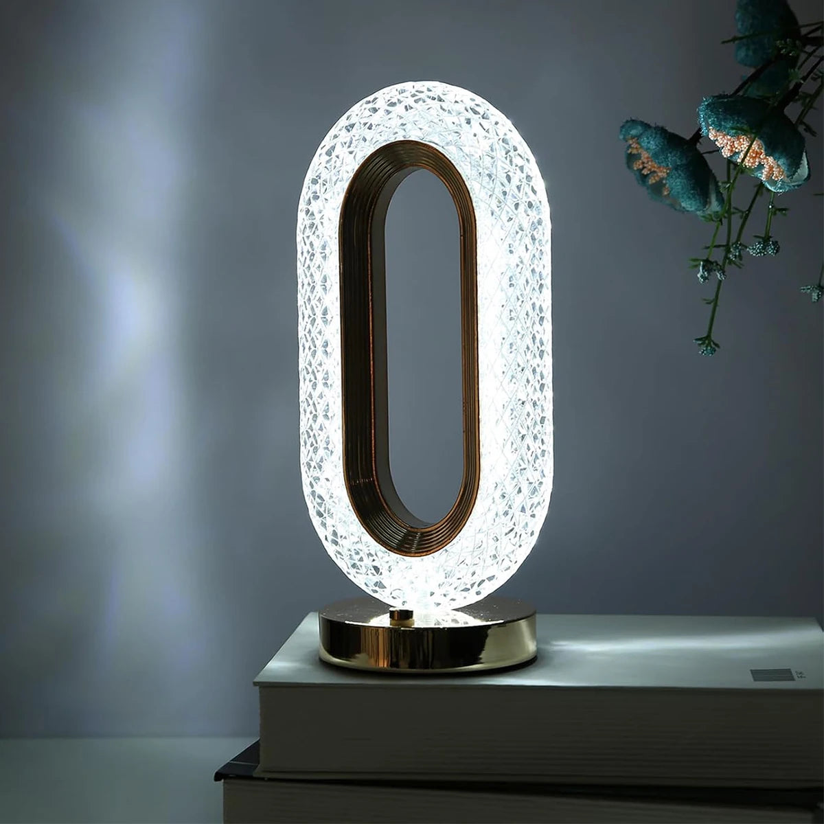 An oval crystal LED table lamp with a gold frame and white diffused light is displayed on a modern surface.