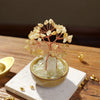 A small natural crystal money tree with a rose quartz base sits on a light surface.