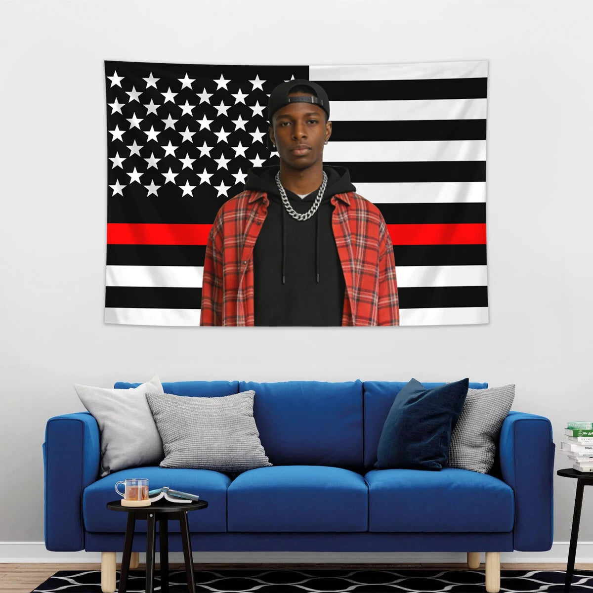 A man wearing a black cap and a black shirt stands in front of an American flag tapestry featuring stars and stripes.