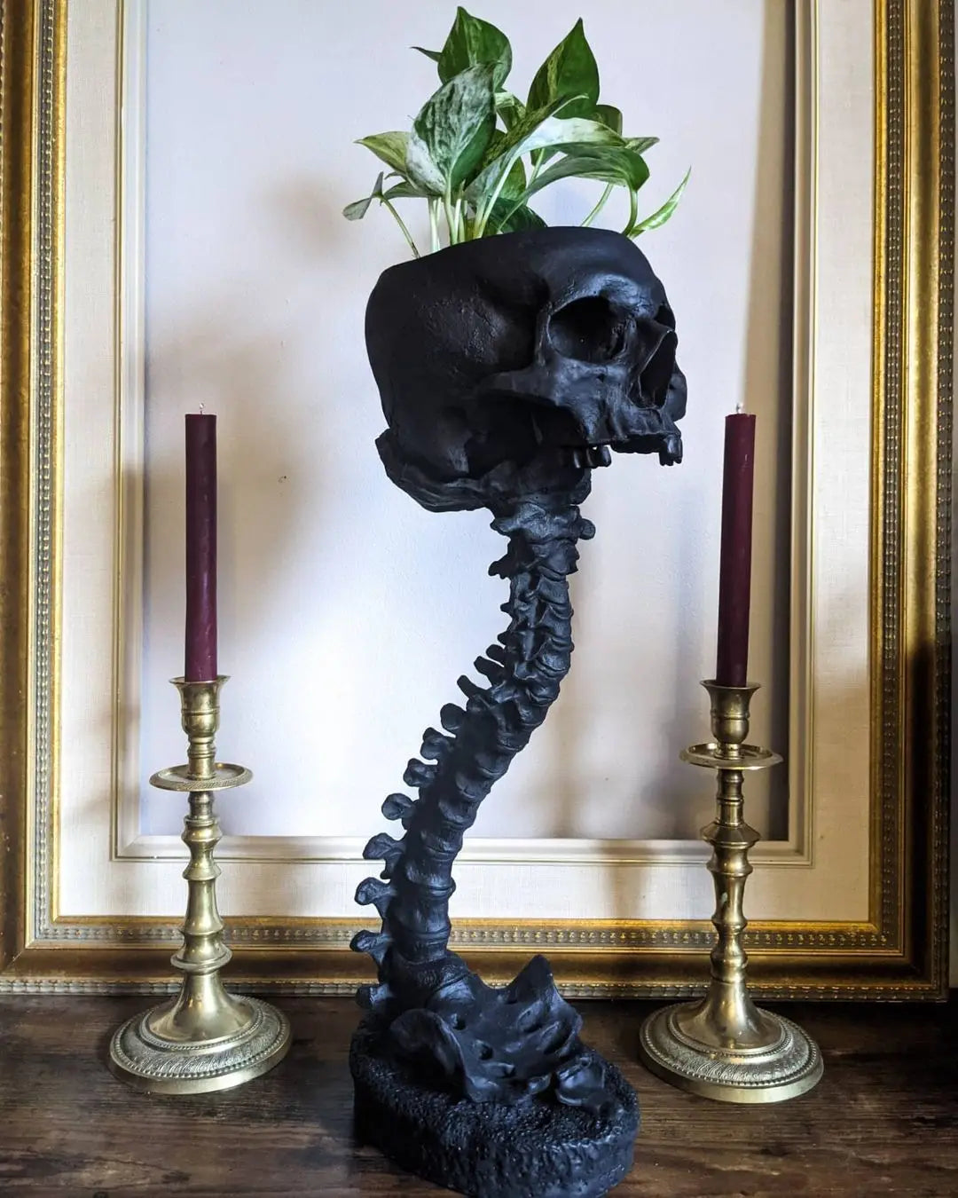 Schwarzes gotisches Schädel-Topfset mit Längenkörper-Design vor einem goldgerahmten Bild.