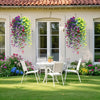 A white outdoor dining set with a table and chairs is placed on a lawn in front of a house decorated with colorful artificial