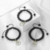 A black beaded bracelet with a gold charm featuring an astrological symbol is displayed on a white box.