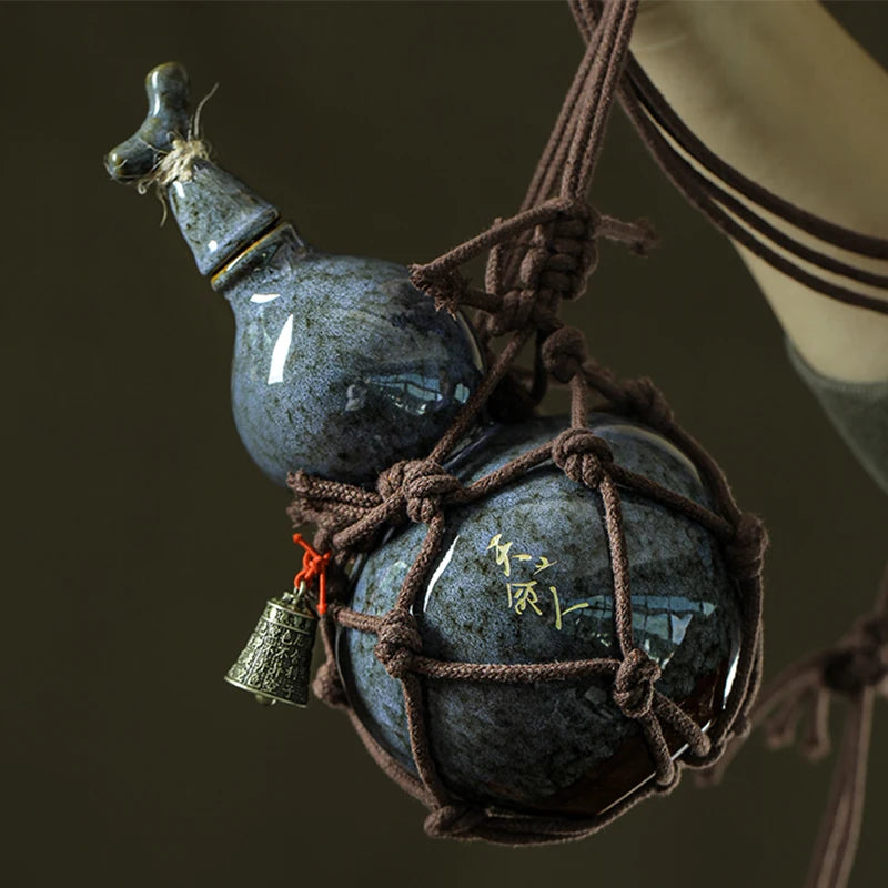 A dark blue ceramic wine gourd with a stopper is suspended by twine, used for hot water or beverages.