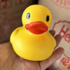 A bright yellow rubber duck bath toy with an orange beak and blue eyes is held in a hand.