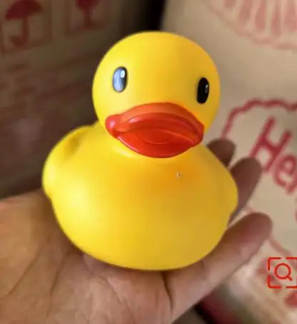A bright yellow rubber duck bath toy with an orange beak and blue eyes is held in a hand.