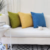 Two solid color linen pillows, one olive green and one mustard yellow, resting on a white sofa.