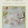 A clear box containing a pink and white artisan tulip bouquet and a soy wax candle.