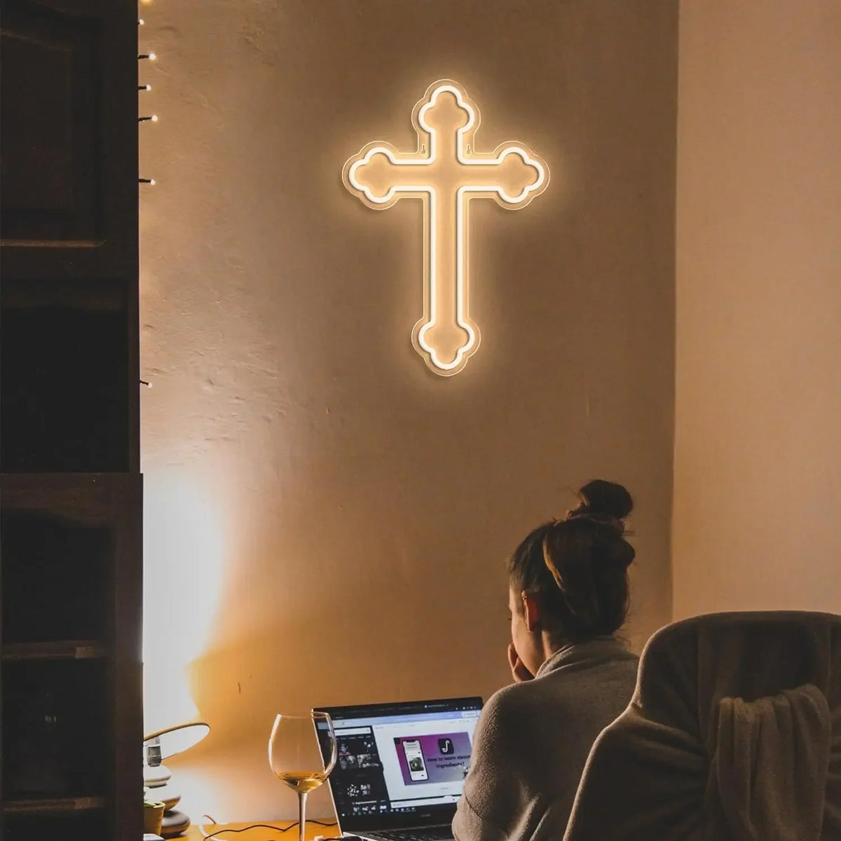A glowing white neon cross wall sign is mounted on a light-colored wall, viewed from the side.