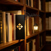 A vintage bookshelf lantern lamp with an ornate black metal bracket illuminating a dark book in a wooden shelf.