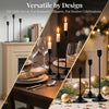 A set of modern black metal taper candle holders with white candles arranged on a wooden table for decorative use.