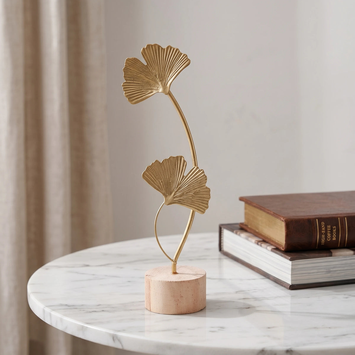 A gold-toned iron ginkgo leaf ornament set with a slender stem displayed on a white marble surface.