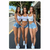Trois jeunes femmes posant dehors en shorts en denim et hauts blancs courts.