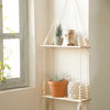A rustic wooden wall shelf with macrame hangers displaying potted plants and decorative items.