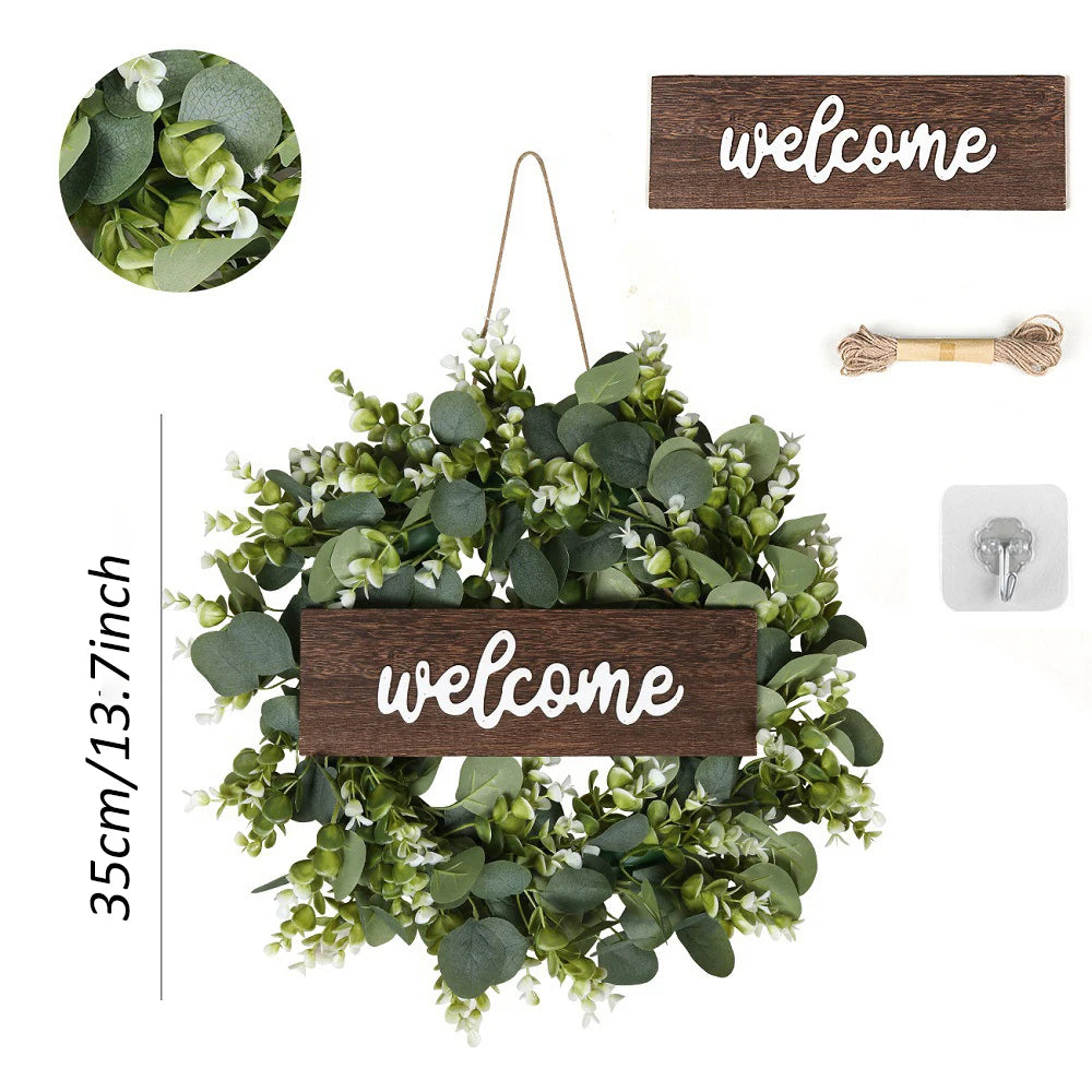Artificial eucalyptus wreath with green leaves and a wooden welcome sign hanging on a wire.