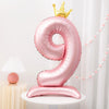 A pink foil balloon shaped like the number 9 with a gold crown on top