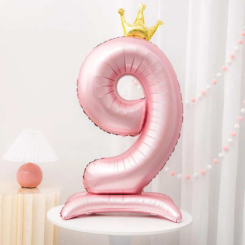 A pink foil balloon shaped like the number 9 with a gold crown on top
