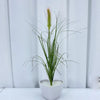 A potted artificial grass plant with thin green stems and a pink flower spike, set against a white background.