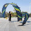 Una persona realiza una danza de dragón con un gran atrezo de dragón azul oscuro y verde en forma de arco al aire libre.