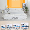 A white queen bed with a white duvet and sheets is shown in a bright room, alongside various sized art prints and a washing m