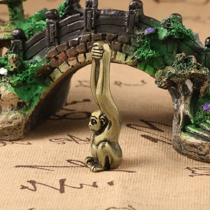 Vintage brass monkey key chain charm standing on a mossy bridge structure.