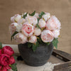 A bouquet of elegant artificial silk peonies in shades of pink and white displayed in a dark vase.