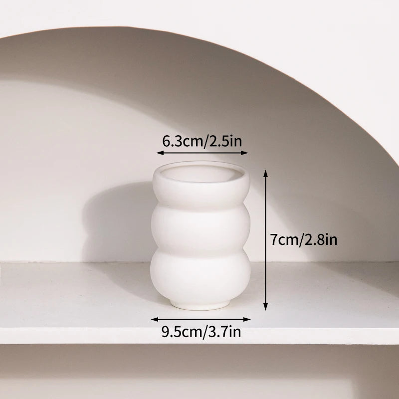 A white ceramic vase with stacked, rounded forms is displayed on a shelf.